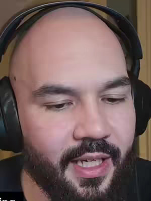 A close-up shot of a bald man with a full beard. He's wearing headphones and is looking slightly towards the camera. The background is out of focus.
