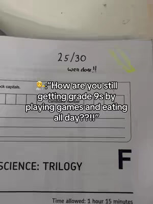 The image shows a close-up of a graded school paper on a desk, with a score of 25/30 and the words "well done!!" written on the top. Below the score is a text overlay containing a question about how someone consistently gets high grades despite seemingly spending their time on games and food. The background suggests a classroom or study environment.