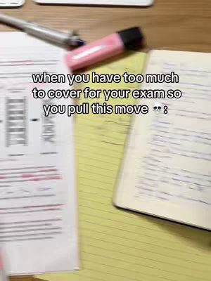 The image shows an overhead view of a desk with study materials scattered across it. There are loose-leaf papers with red and black markings and a notebook open with handwritten notes in blue. A pink highlighter and a pen are visible, and the colors are muted.