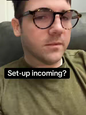 A man with fair skin and short brown hair is centered in the frame. He's wearing glasses with tortoiseshell frames. He has a small amount of stubble.  He's wearing a green colored shirt. The background is a muted gray tone. Black text overlay with the words 'Set-up incoming?' is in a white box at the bottom of the image.