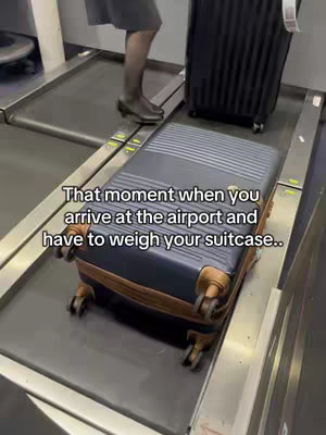 The cover image shows a suitcase placed on a baggage scale at the airport. A person in a dark skirt and boots stands beside the scale. Text overlayed reads: 'That moment when you arrive at the airport and have to weigh your suitcase.'
