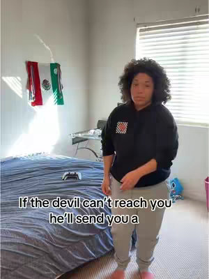 The cover image shows a young woman standing in a bedroom. She is wearing a black hoodie and gray sweatpants and has curly hair. Behind her, there's a bed with a blue comforter, a window with blinds, and a Mexican flag hanging on the wall.