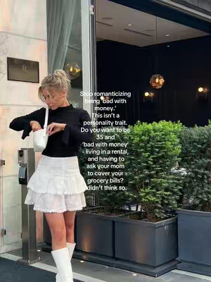 A woman in a black top and white skirt stands outside in a well-lit area with text overlaid on the right. The text discusses avoiding romanticizing being bad with money. The setting appears to be a business or office building.
