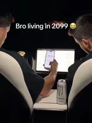 The cover image shows two men from the shoulders up, seated inside a vehicle with black interior. One man in the foreground holds a phone displaying a white screen. In the central area between them is a laptop screen showing a website and a silver Monster energy drink can. The men appear to be in a car setting, judging by the seats and central console.