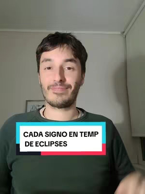 A medium shot shows a fair-skinned man with dark hair and a beard. He is wearing a green sweater and is positioned in front of a neutral backdrop. There's a text overlay on the bottom with the text in white over a colored background.