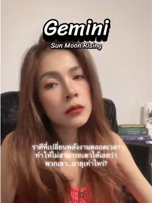 A woman with light skin and long brown hair is centered in the frame. Text overlays at the top, with the word "Gemini" and the text "Sun Moon Rising". The woman has a neutral expression and is looking at the camera. She has lipstick, and wears a pink top. Behind her is a dark chair and a few items placed on a shelf.