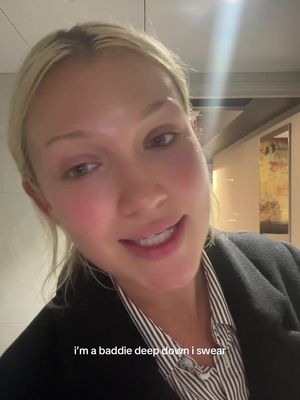 A close-up shot shows a woman smiling slightly, with blonde hair pulled back. She's wearing a black blazer over a striped shirt. Text overlays on the bottom, near her left shoulder.