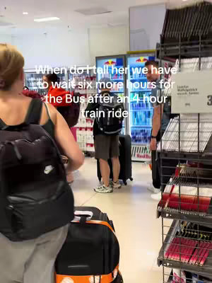 A busy airport scene with multiple people, luggage, and shopping displays. The central figure, a woman with blonde hair, faces the camera with a backpack, while additional people and luggage fill the background.
