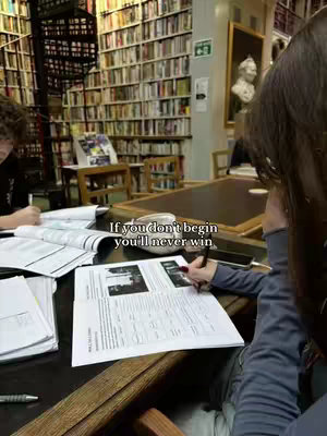 The cover image shows a person writing on a document at a table in a library, with books on shelves in the background. The focus is on the document and the person's hand holding a pen.