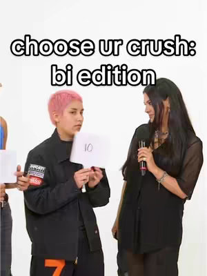 The cover image is a shot of a video set. It features three persons, two of them a woman and a non binary person holding a card. The layout has text overlayed at the top which reads "choose ur crush: bi edition". The overall color scheme is neutral with a white background, black and pink for the people shown, the clothes they wear and white for the card they hold.