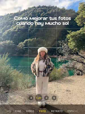 A woman poses in front of a lake and a mountain. She is wearing a white hat, a fur-like jacket, and white pants. She is standing in front of a grid, which looks like a camera app interface. The background includes a serene lake and a lush green mountain. The colors are natural, with a focus on the green of the trees and the blue/turquoise water. The layout is centered: the woman is centered, with the lake and mountains in the background.