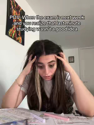 A young woman with long brown hair is the focus, appearing stressed with her hands on her head. She is seated at a desk strewn with papers, pens, and a pink highlighter. Text overlay at the top explains the context.