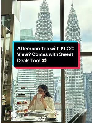 A woman enjoys afternoon tea at a table set near a large window that frames the Petronas Twin Towers in Kuala Lumpur. A black rectangular text box at the top contains white text with the video's title.