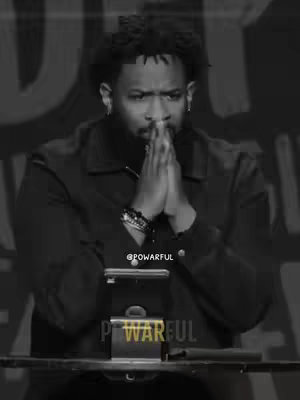 A black and white image of a Black man with short, textured hair, is positioned in front of a plain background of graduated tones. The man is the central focus, with his hands clasped in front of his face in a praying gesture, lips slightly parted revealing teeth, eyes looking downwards, conveying a sense of seriousness. Dark clothing and close-up shot emphasize his facial expression, and text overlays.
