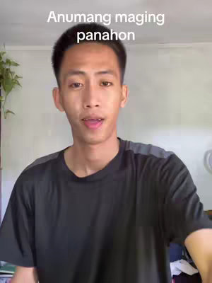 A young man with short, dark hair is centered in the frame, facing the camera with an open mouth as if speaking. He's wearing a black t-shirt with gray shoulder accents against a white background, possibly a wall. Above him, the following text is displayed: Anumang maging panahon