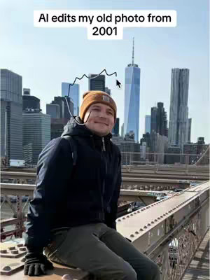 A man wearing a winter hat and jacket sits with his legs dangling over a bridge while facing the camera. In the background, the New York City skyline is visible, including the One World Trade Center.