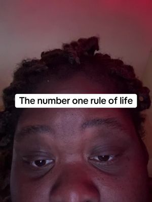 The cover image is a close-up shot of a person's face, with the focus on the eyes and lower face. The person has dark skin and dark, possibly locs hairstyle. Above their head is illuminated by a red-toned light. A text overlay positioned at the midpoint reads, "The number one rule of life".