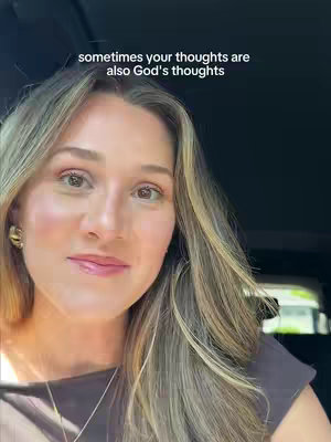 A selfie-style shot with a woman in the foreground looking slightly upward, with text at the top. The woman has long, highlighted blonde hair, with a soft, natural makeup look. She is wearing a dark brown top, and gold hoop earrings. The background is dark.