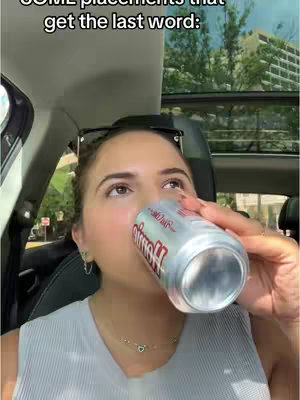 A woman inside a car is drinking from a can. The camera angle includes the car interior, the side window, and the scenery outside. Overhead text adds a caption. The woman has sunglasses on top of her head and is in the front seat.
