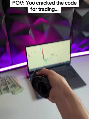 A top-down shot shows a laptop displaying a stock chart, in a hand holding a belt roll. Cash and a modern designed backdrop are on the white desk.