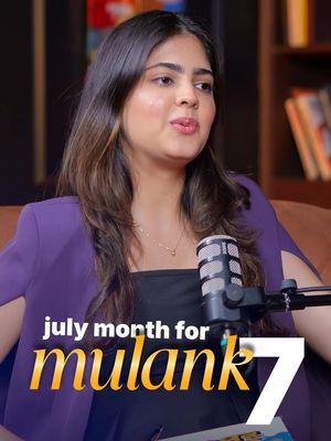 A woman with long, dark hair wearing a purple blazer is seated in front of a blurred background, possibly a bookcase. A microphone is positioned in front of her. Overlayed on the image is text in a gold color, advertising the video's context.