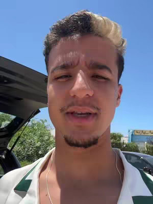 The cover image features a young man with light skin, visible pores, and a slightly furrowed brow, suggesting a focused or thoughtful expression. He has dark hair with blonde highlights on top and is clean-shaven with a short dark mustache and goatee. His eyes are dark, and he has a light shadow. The background is a vibrant blue sky and parts of a car are visible, hinting at an outdoor setting, probably a sunny day.