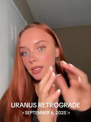 A close-up shot of a woman with long, reddish-blonde hair and light eyes. She is wearing a black top and gold earrings. The background is a neutral wall with a white door frame visible on the left. Text overlay at the bottom of the image reads "URANUS RETROGRADE ✨ SEPTEMBER 6, 2025✨".