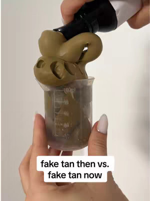 The image shows a hand holding a beaker filled with a dark brown liquid, with a blob of a lighter brown substance pouring into it. A black and white bottle is pouring the substance. The background is a plain white surface.