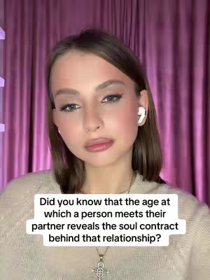 A woman with light skin, wearing a beige sweater and white earbuds, looks at the camera with a neutral expression against a blurred pink curtain background. Text on a white box in the lower part of the image reads: 'Did you know that the age at which a person meets their partner reveals the soul contract behind that relationship?'