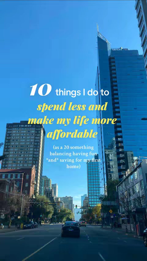 An urban landscape with a bright blue sky. The perspective is from a street level, with a road leading towards the background. Tall buildings, including skyscrapers, line both sides of the street. The sky is clear, and the overall feel is bright and airy. Text overlays are present, indicating the video's focus on saving money and affordability.