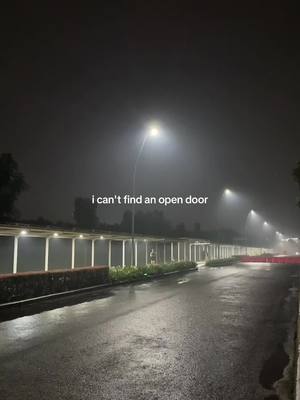A nighttime shot of a wet road curving into the distance. Streetlights illuminate a covered walkway and the road. The sky is dark and slightly foggy. Text is overlaid on the image.