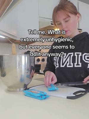 A person in a kitchen is cutting and slicing small blue wrapped items on a white cutting board. The person is wearing a black hoodie with white lettering. The text overlay asks a question about unhygienic practices.