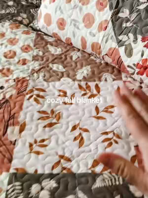 The cover image shows a close-up of a fall-themed patchwork quilt. The quilt is made up of various squares with different patterns and colors, including floral prints in peach and white, brown and tan geometric shapes, and leaves.