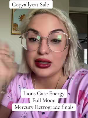 A woman with blonde hair and large glasses sits in front of a camera. Text overlays are present at the top and bottom of the screen.