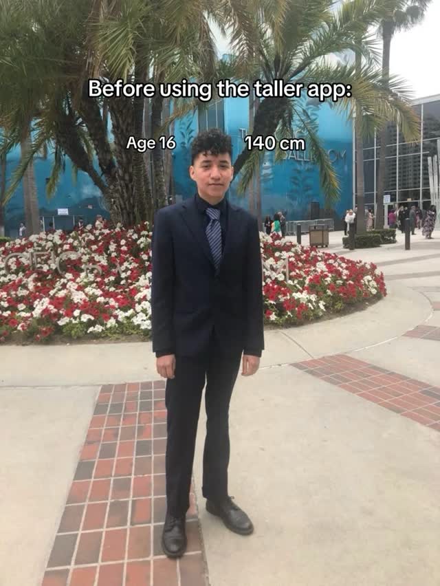 A young man in a dark suit stands in front of a flowerbed and palm trees. Text overlays indicate the age and height before using an app. The setting is a public space with buildings in the background.