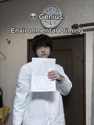 A person holding a paper with a drawing, standing in front of a wall. The text overlay features the words "Genius: Environmental Priming" and an alien emoji above the person.