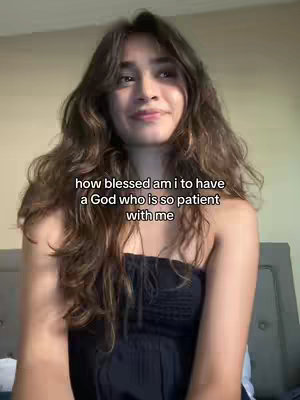 A young woman with long, wavy brown hair and a light complexion is centered in the frame. She is wearing a black tube top and has a subtle smile, looking towards the upper left of the image. The background is a neutral beige color. The text "how blessed am i to have a God who is so patient with me" is displayed in a white font across the image.