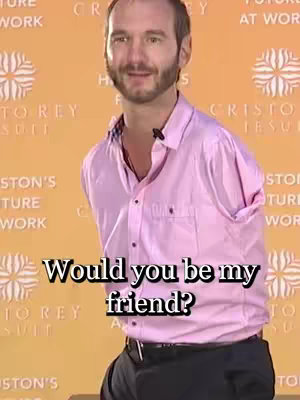 A man in a pink shirt stands in front of a blurred background. The man has no arms. Text overlayed on the image asks, "Would you be my friend?"