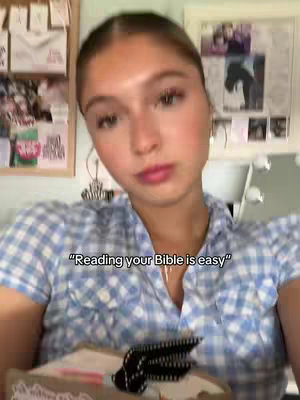 A young woman with light skin and blonde hair is centered in the frame, looking slightly up towards the camera. She has a soft expression, light pink lip color, and large, round hoop earrings. She is wearing a blue and white checkered button-down shirt. Behind her is a cluttered background with framed pictures, notes, and other decor on the wall.