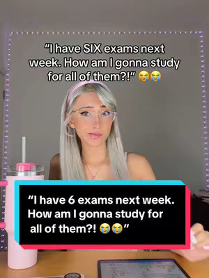 A woman with long silver hair and glasses is centered in a selfie-style video. The background is a plain, light-colored wall. The woman wears a white top and a pink headband. In the bottom section, a text bubble contains the phrase "I have 6 exams next week. How am I gonna study for all of them?!," followed by emojis. Drinks and tech devices are on a wooden surface below.