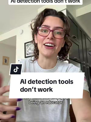A selfie-style shot of a young woman indoors, speaking directly to the camera with a smile. She wears eyeglasses with a pink frame and has short curly hair. The background includes items associated with a home, such as a picture frame and cabinets to the right. There is a white rectangle overlaying the bottom middle of the screen with text, similar to a title.