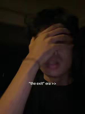 A person is seen covering their face with their hand, appearing emotional. The lighting is dim, and the background is blurred. The overlay text "the exit" era >> is placed at the bottom of the frame.