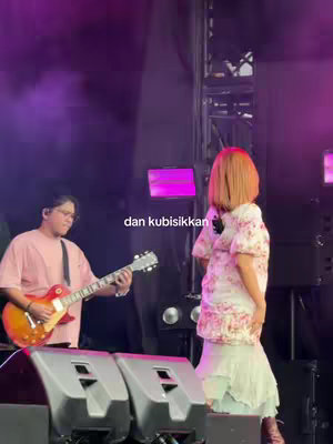 A live performance stage is shown with an artist singing into a microphone, and a guitarist playing the guitar. The stage is lit with purple and pink lights.