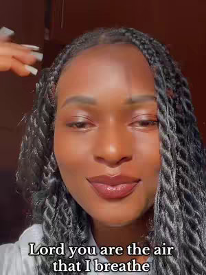 Close-up shot of a woman with dark skin and braided hair. She is looking towards the camera with a gentle expression. The background is a soft, warm brown. Text at the bottom reads "Lord you are the air that I breathe".