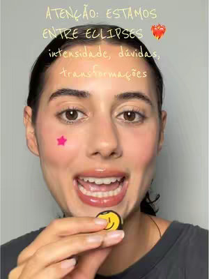 A person with minimal makeup, a pink star sticker on their left cheek, and a small smiley face accessory is shown. The person is smiling with their mouth open, and the image has text overlays.