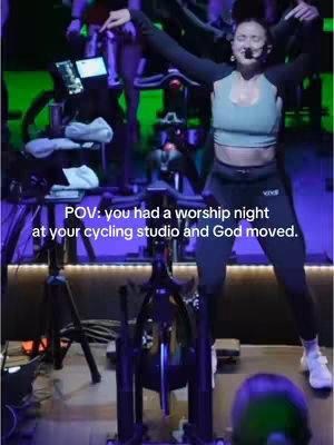 Cover image of a woman in activewear leading a cycling class. She has her arms raised and is smiling, with a microphone headset.  A cycling bike is prominent in the foreground, and other cyclists are visible in the background. Text overlayed at the bottom.