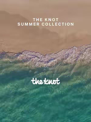An aerial, top-down view depicting a beach and ocean split diagonally across the frame. The top portion shows a sandy beach, with a light brown hue. Adjacent to it, the water's edge displays white foamy waves, transitioning to streaks of teal and blue, representing the ocean. The bottom area showcases the ocean in shades of turquoise. White text, "THE KNOT SUMMER COLLECTION", is placed prominently in the top center, while the logo "the knot" is placed in white cursive at the center bottom. The image has a clean, inviting aesthetic with a clear focus on the beach and ocean.