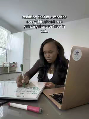A woman is sitting at a desk, writing on a whiteboard while looking at her laptop, in a well lit room. Text overlayed on the image.