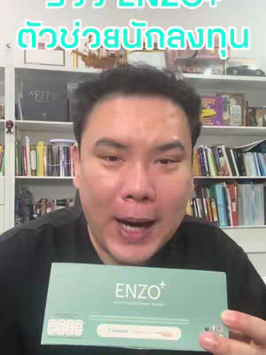 A man with a slightly chubby face smiles at the camera while holding a product box. The box, labeled 'ENZO+', is light green and white. He is standing in front of a bookshelf filled with books and decorative items.
