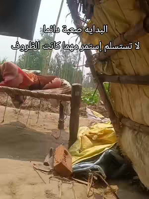 A scene captured outdoors shows a bed set up in a rudimentary shelter, with a person lying down under a blanket or sheet. The setting appears rustic and simple, possibly suggesting a rural or underdeveloped location, and the image is overlaid with Arabic text.